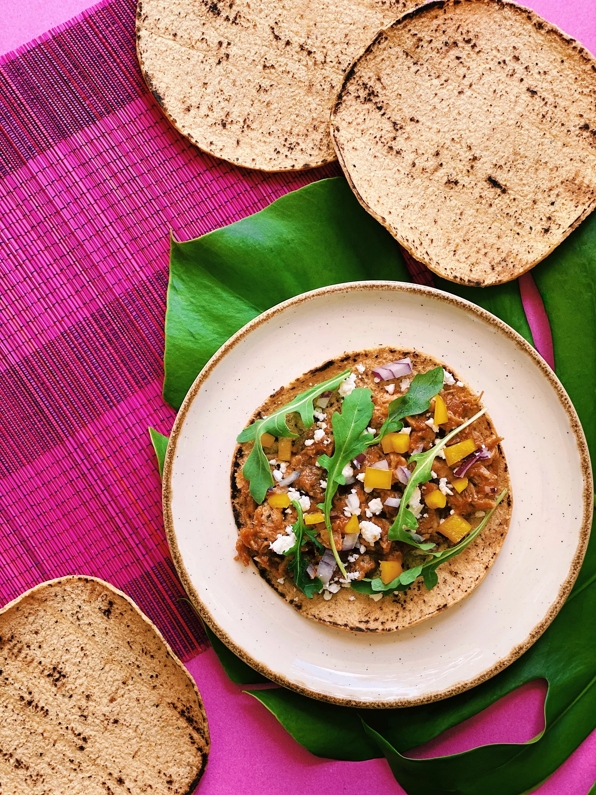 A crisp corn tostada, topped with diced seasonal goodness, crumbled cheese, and fresh greens
