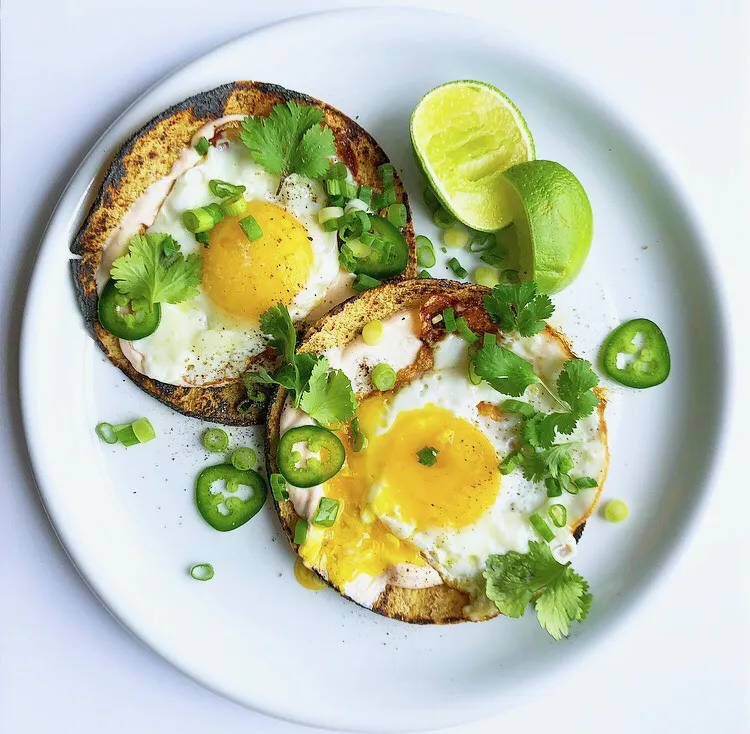 Breakfast tacos on warm corn tortillas, topped with eggs and fresh herbs