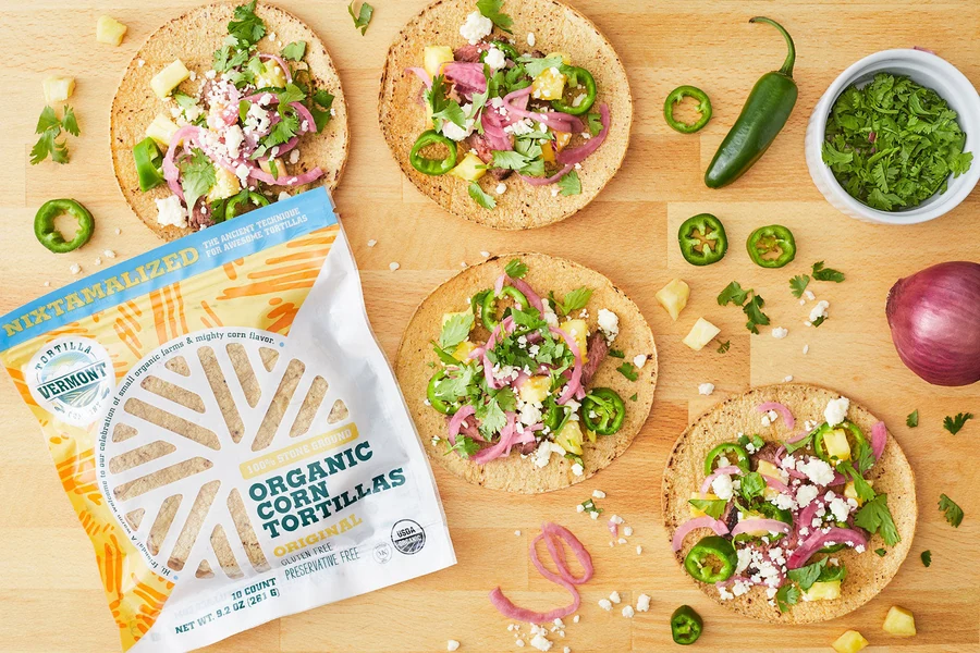 Open tacos with colorful toppings beside Vermont Tortilla Company Original tortilla packaging