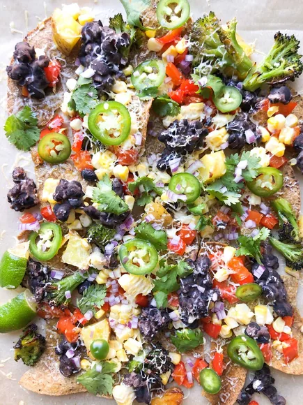 A tray of corn tortilla nachos with beans, vegetables, and herbs