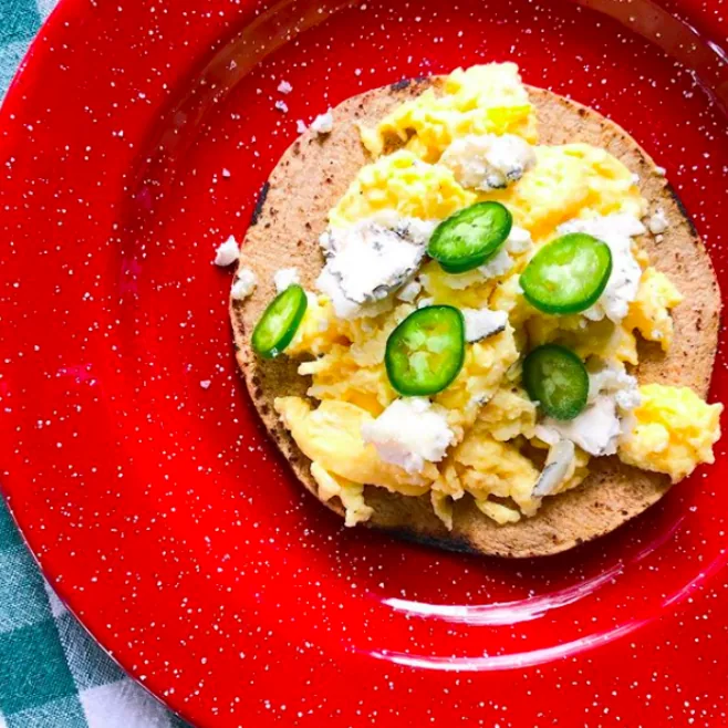 A corn tortilla topped with fluffy scrambled eggs, crumbled cheese and fresh jalapeño on a red plate