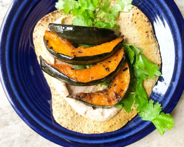 Corn tortilla topped with roasted acorn squash and cilantro on a blue plate