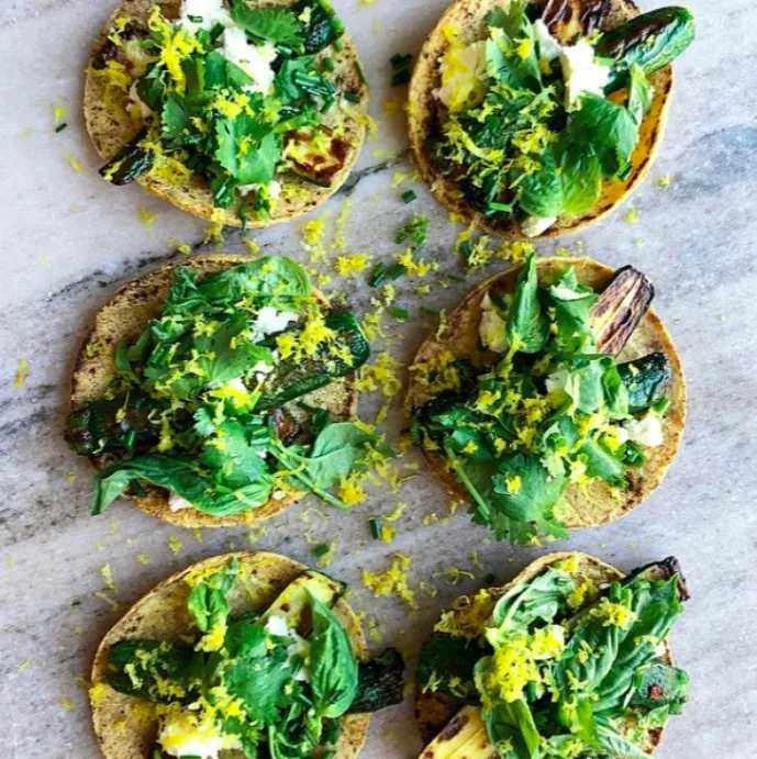 Small corn tortilla tacos with browned baby zucchini halves, crumbled feta, mixed fresh herbs and lemon zest