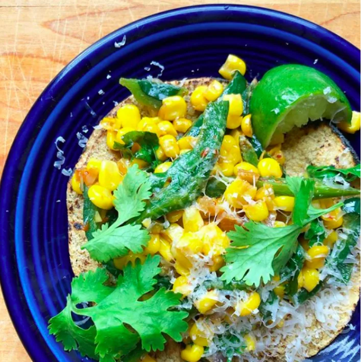 Corn tortilla topped with sweet corn, sautéed poblano strips, finely grated cheese and cilantro beside a lime wedge