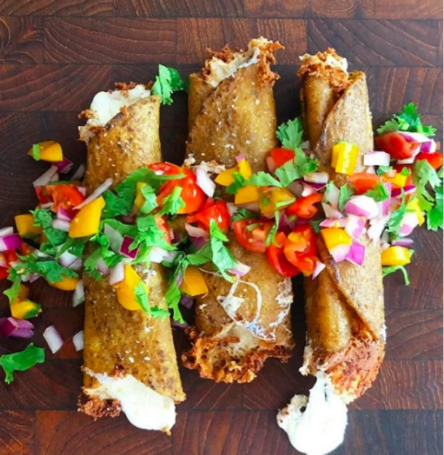 Golden rolled corn tortilla taquitos with melted white cheese and a colorful tomato, red onion and cilantro topping