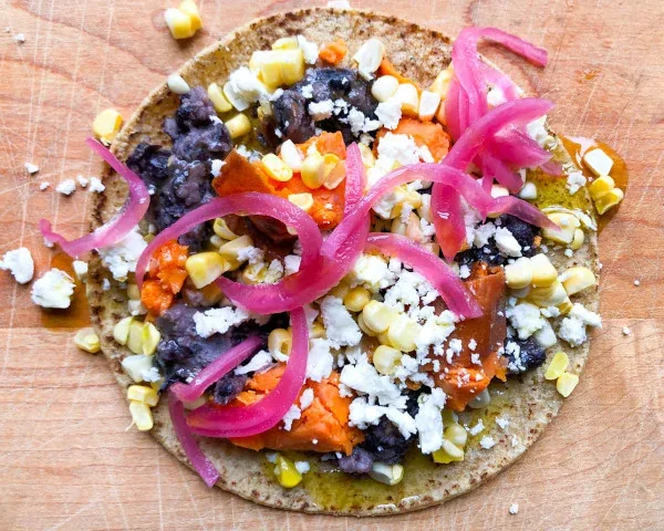 Corn tortilla topped with black beans, corn, pickled red onion and crumbled cheese