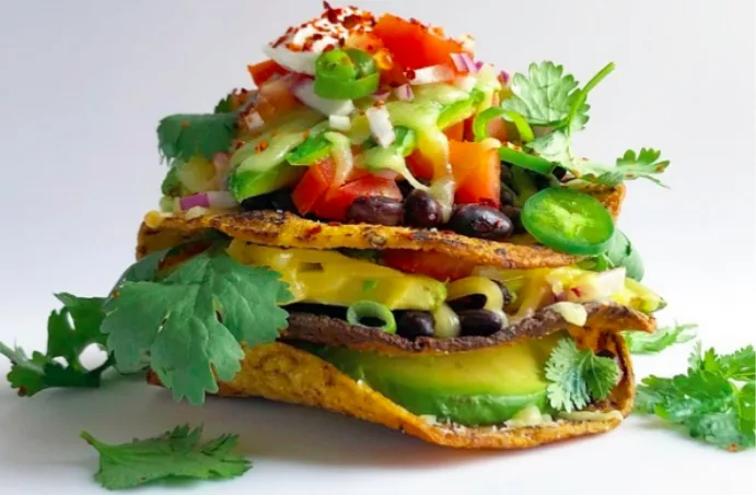 Three-layer crisp corn tortilla stack filled with black beans, avocado, cheddar and vegetables, topped with sour cream