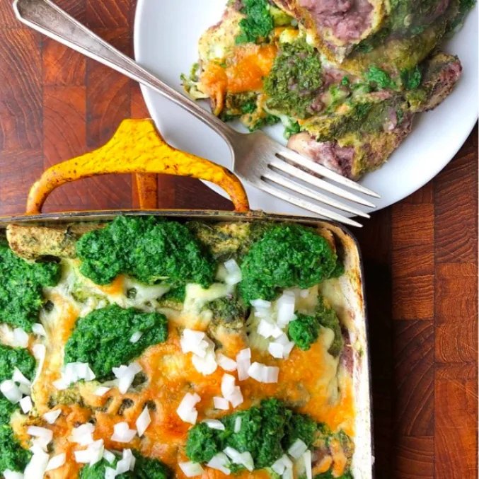 Baked corn tortilla enchiladas with black bean filling, melted cheddar, bright cilantro sauce and diced white onion