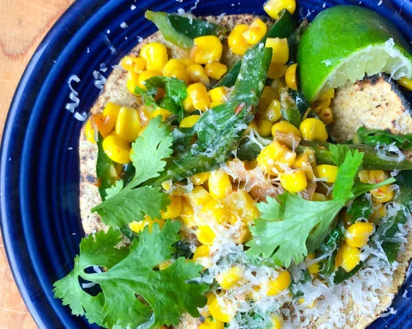 Corn tortilla topped with sweet corn, peppers, cilantro and grated cheese beside a lime wedge