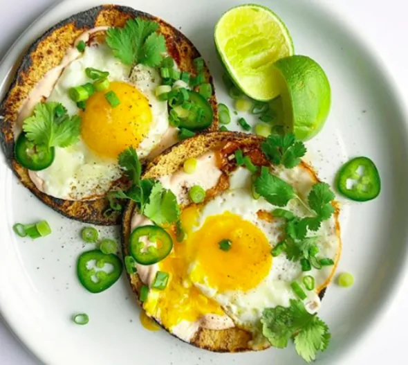 Open corn tortilla breakfast tacos with fried eggs, scallions, sliced jalapeño, cilantro and lime wedges