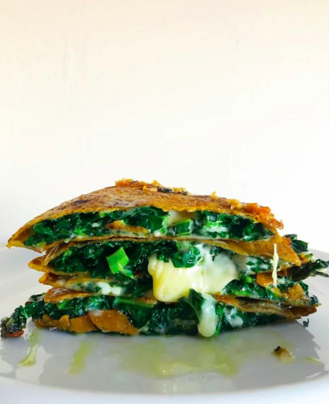 Stacked wedges of golden corn tortilla quesadillas filled with green kale and melted cheese