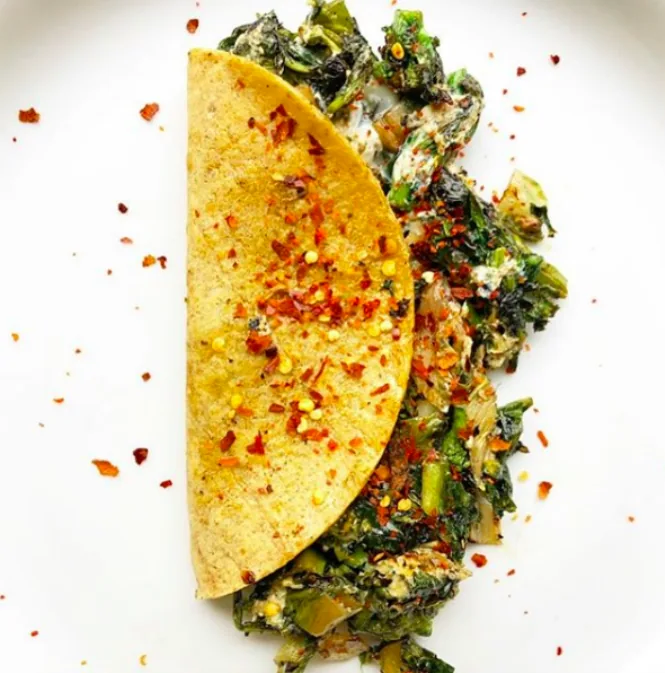 Crisp folded corn tortilla filled with egg, leafy greens and melted cheese, sprinkled with chili flakes