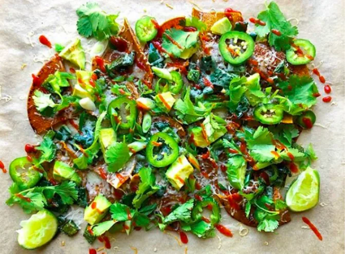 A tray of turmeric corn tortilla nachos with melted white cheddar, avocado, jalapeño slices, cilantro and lime