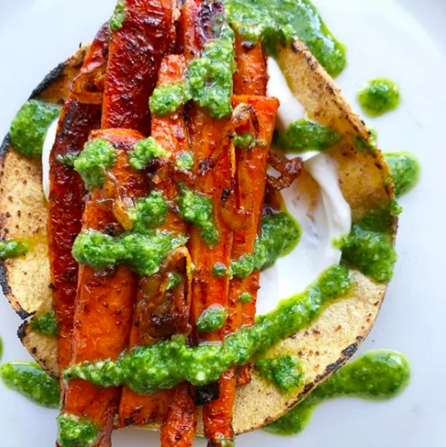 Corn tortilla topped with yogurt, browned roasted carrot strips and bright green cilantro salsa verde