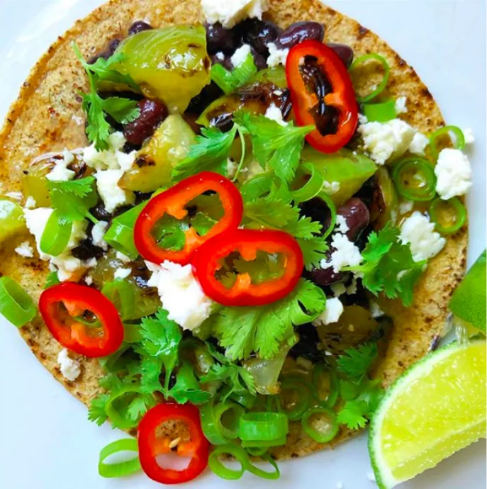 Corn tortilla topped with charred green tomatillos, black beans, cotija, scallions, cilantro and red Fresno chile rings