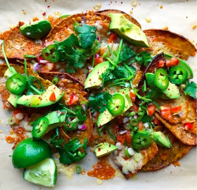 Cheese-covered corn tortilla nachos with avocado slices, jalapeño, diced tomato and red onion, cilantro and lime