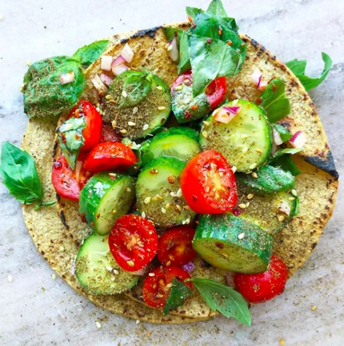 Corn tortilla topped with sliced cucumbers, grape tomatoes, diced red onion, fresh basil and za’atar
