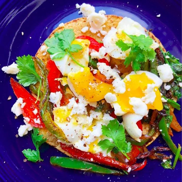 Corn tortilla covered with sautéed red and green peppers, onions, smashed boiled egg, crumbled feta and cilantro