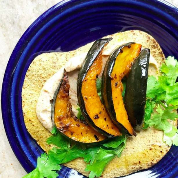 Corn tortilla topped with chipotle yogurt, cilantro and roasted acorn squash wedges on a blue plate