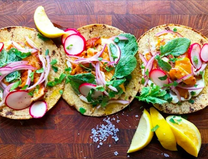 Corn tortilla fish tacos with tilapia, sliced radishes, red onion and fresh greens, served with lemon wedges