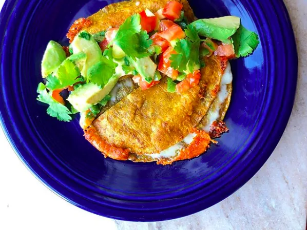 Golden cheese quesadillas topped with avocado, tomato and cilantro on a blue plate
