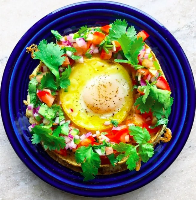 Round corn tortilla and melted cheddar stack with an egg in the center, surrounded by tomato salsa and cilantro