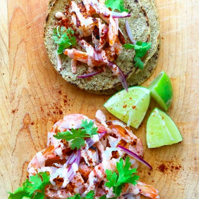 Corn tortillas topped with creamy grilled shrimp, thin red onion slices and cilantro, with lime wedges alongside
