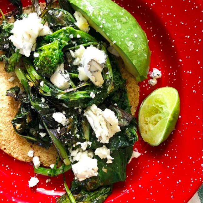 Corn tortilla with wilted kale and broccoli rabe, crumbled goat cheese, avocado slices and a lime wedge