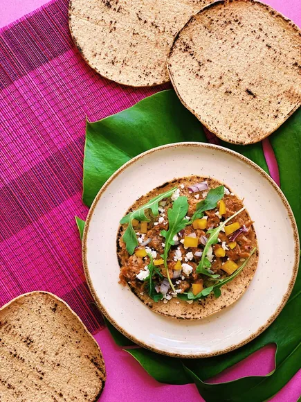 A tostada topped with vegetables, crumbled cheese, and fresh greens