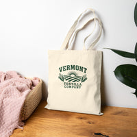Fields & Sun natural canvas tote, resting on a wooden bench beside a basket and plant